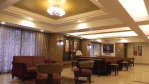 A spacious lobby with a high ceiling, chandeliers, and a seating area with sofas and chairs. - Hotel Reeva Suites (Rahata)