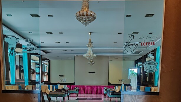 A hotel lobby with a large, circular floor design, a chandelier, and a reception desk with a coffee-themed sign. - Hotel Reeva Suites (Rahata)