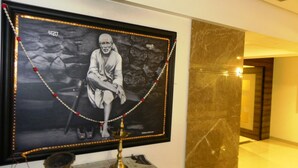 A framed portrait with a decorative border and a small lamp below it, set against a marble wall. - Hotel Reeva Suites (Rahata)