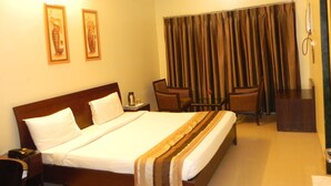 A hotel room with a large bed, a desk, a chair, and a window with curtains. - Hotel Reeva Suites (Rahata)