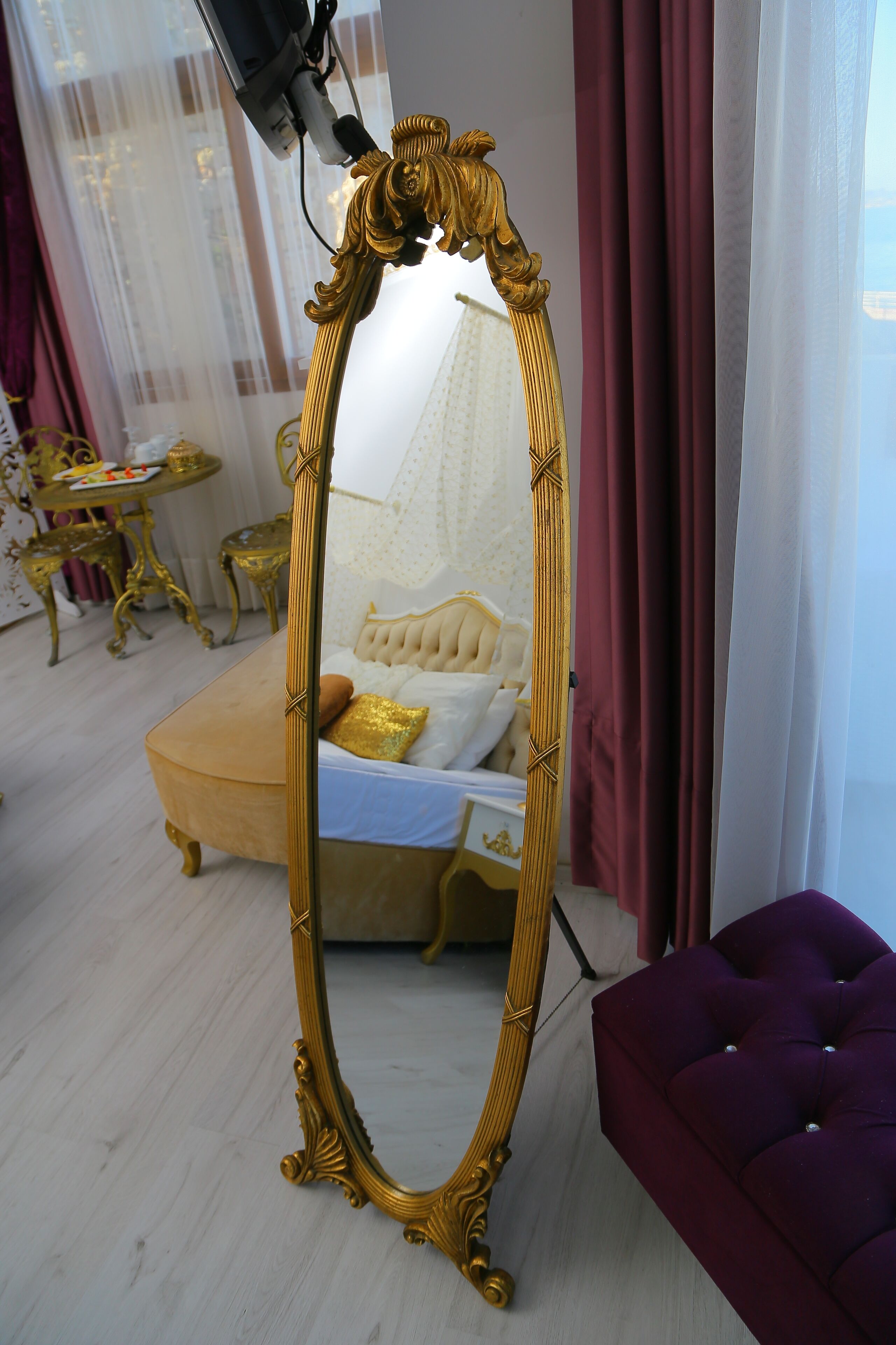 Um quarto com um espelho grande e ornamentado, um sofá com capitonê e uma pequena mesa redonda.