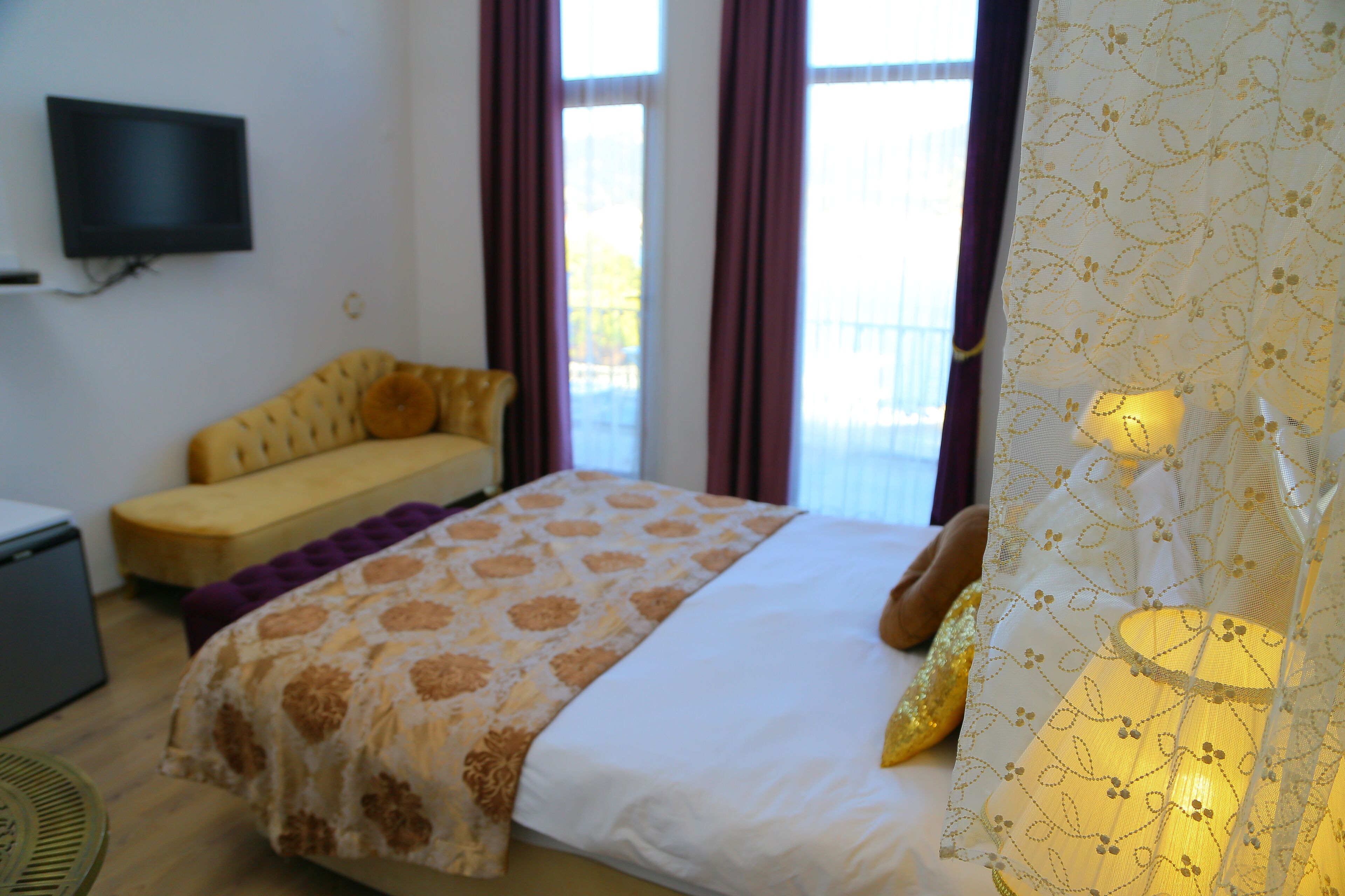 A bedroom with a bed, a sofa, a TV, and a window with curtains.