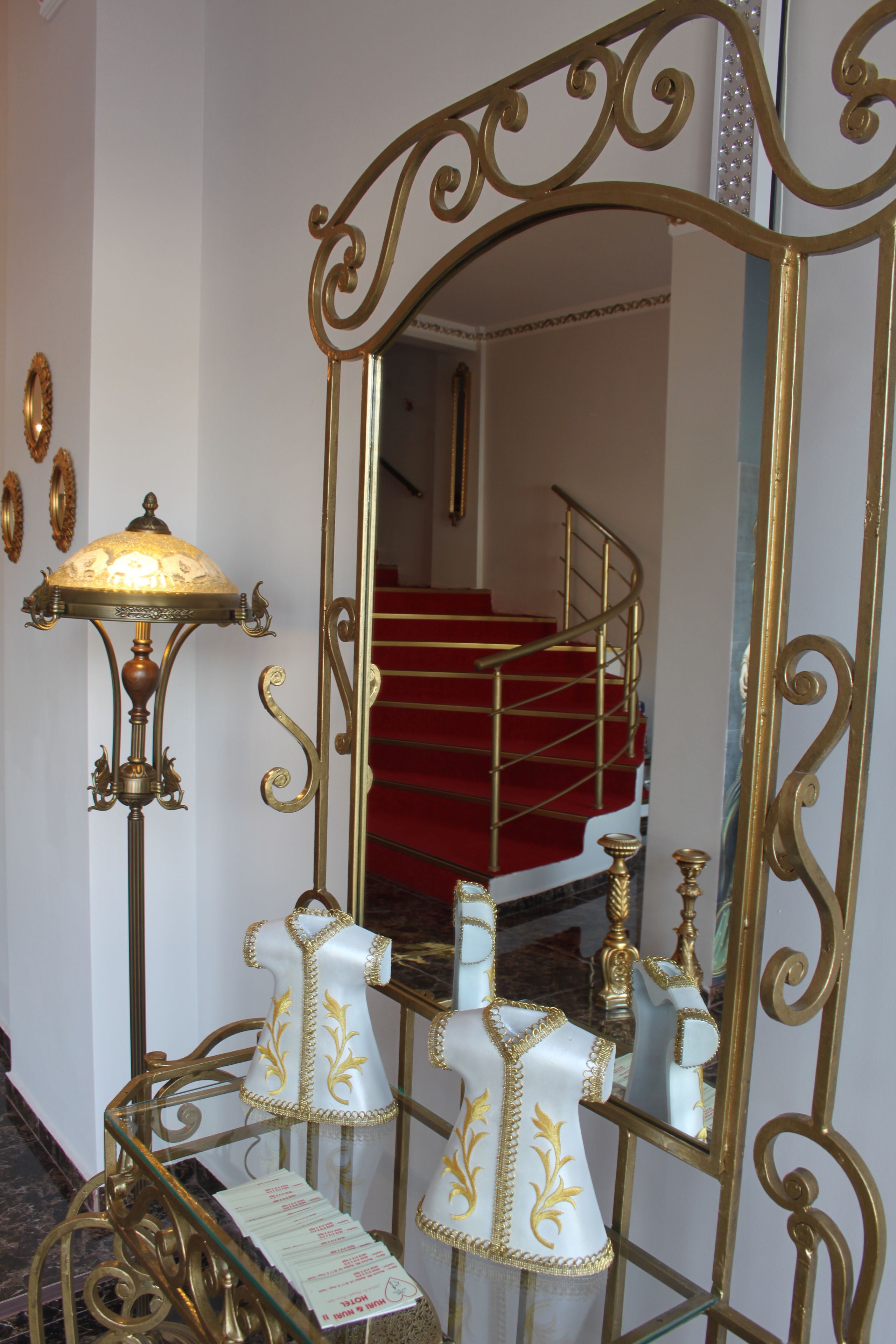 A room with a large ornate mirror, a red carpeted staircase, and a decorative lamp.