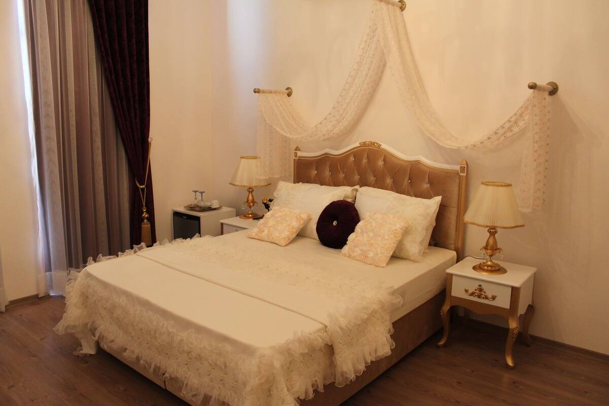 A large bed with a canopy, two bedside tables with lamps, and a wooden floor.
