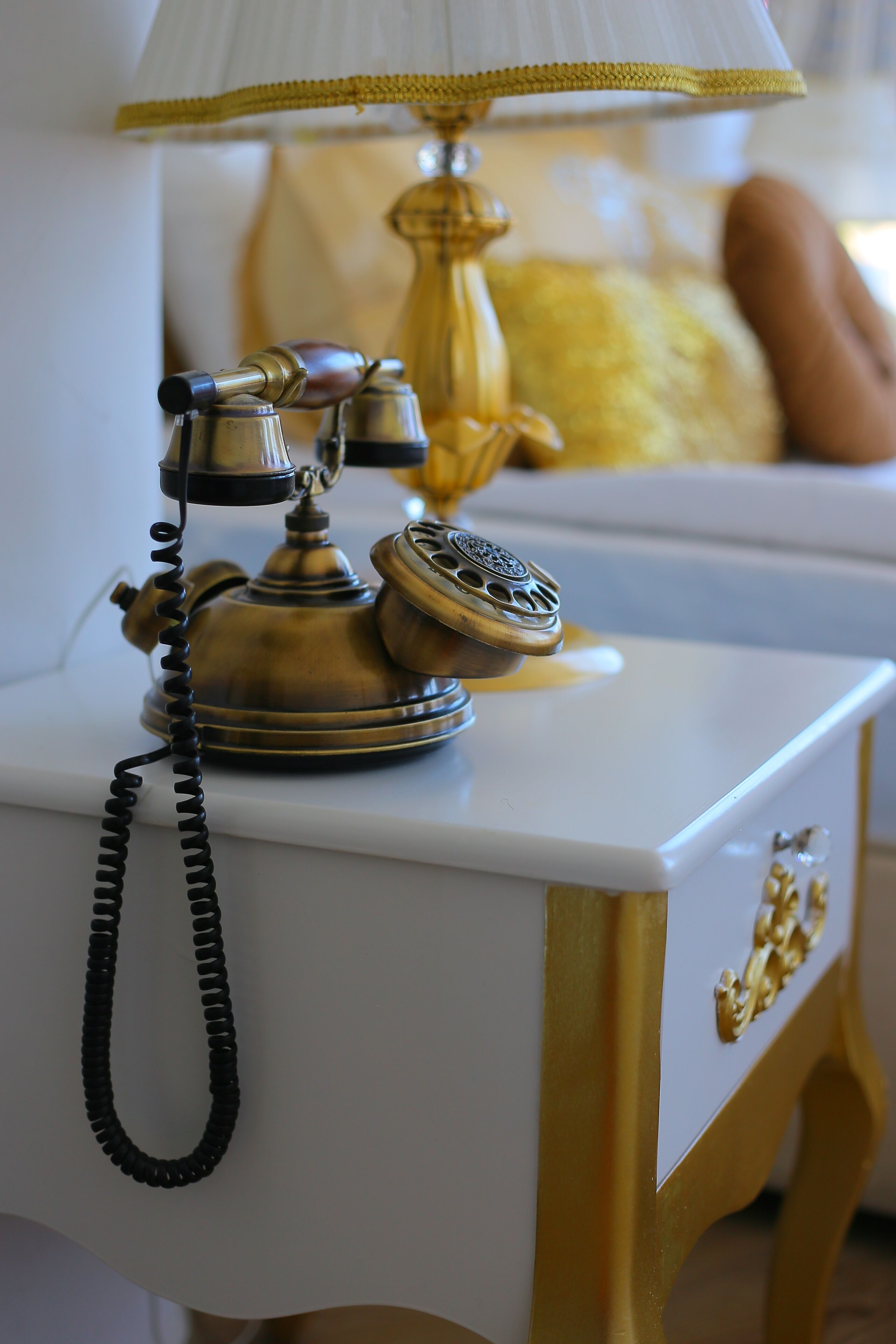 A vintage telephone on a bedside table with a lamp and a decorative item.