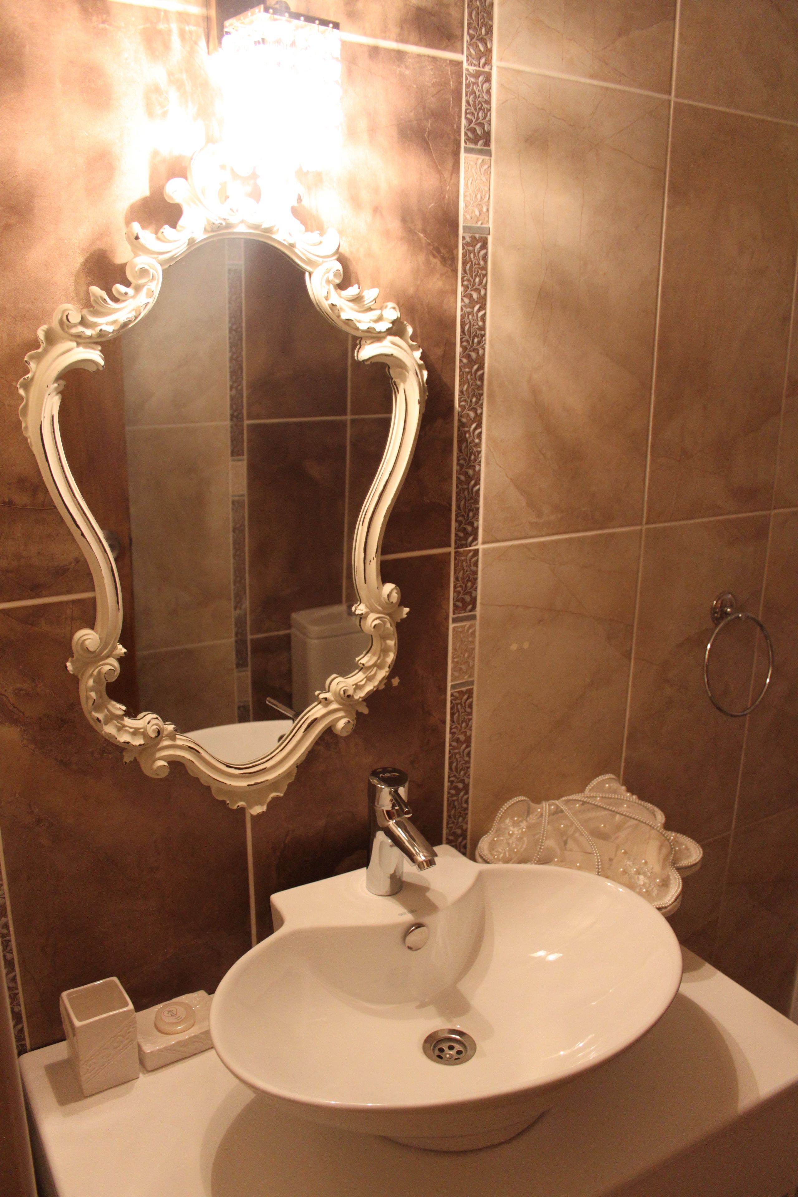 A bathroom with a white ornate mirror, a white sink, and a towel rack.