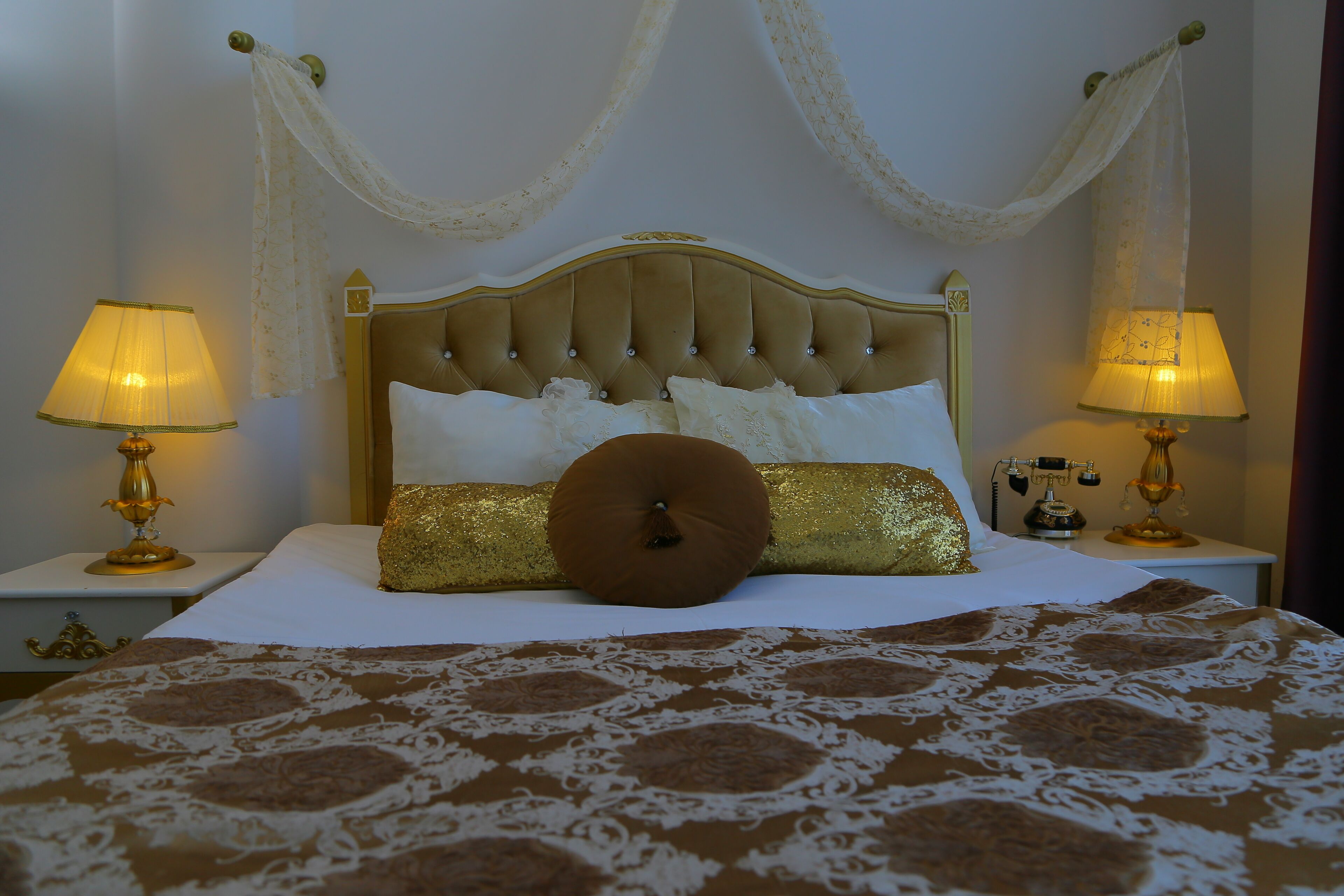 A neatly made bed with a patterned bedspread, two bedside lamps, and a decorative headboard.