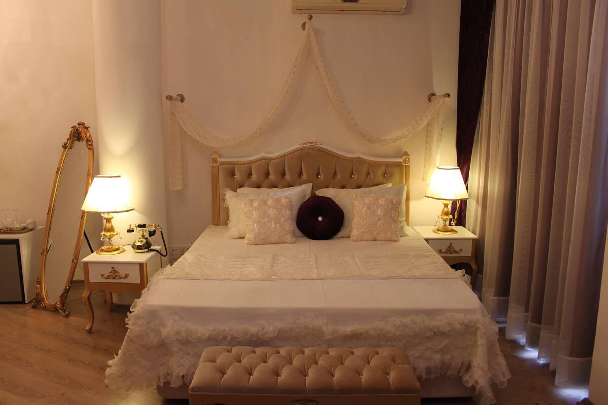 A bedroom with a large bed, two bedside tables with lamps, a mirror, and a canopy over the bed.