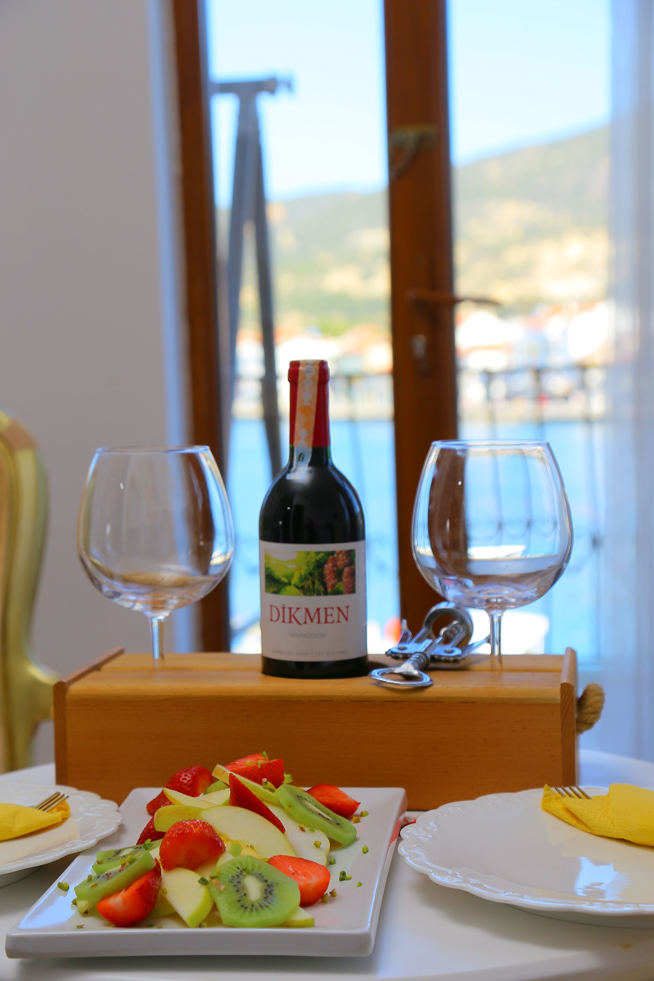 A table with a bottle of wine, two glasses, and a plate of fruit salad.