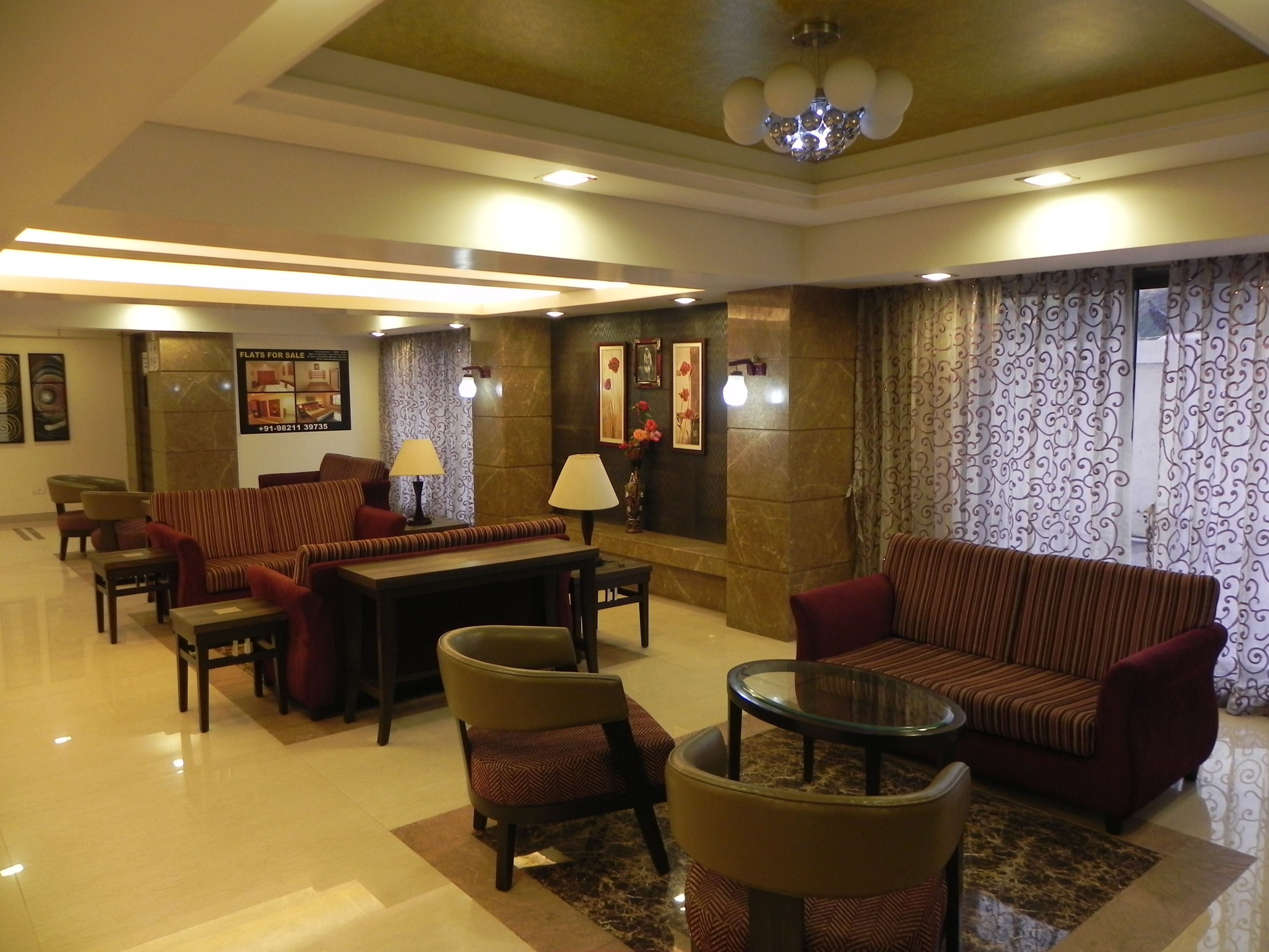A spacious lobby with a sofa set, a coffee table, and chairs. There is a wall with a framed picture and a lamp.
