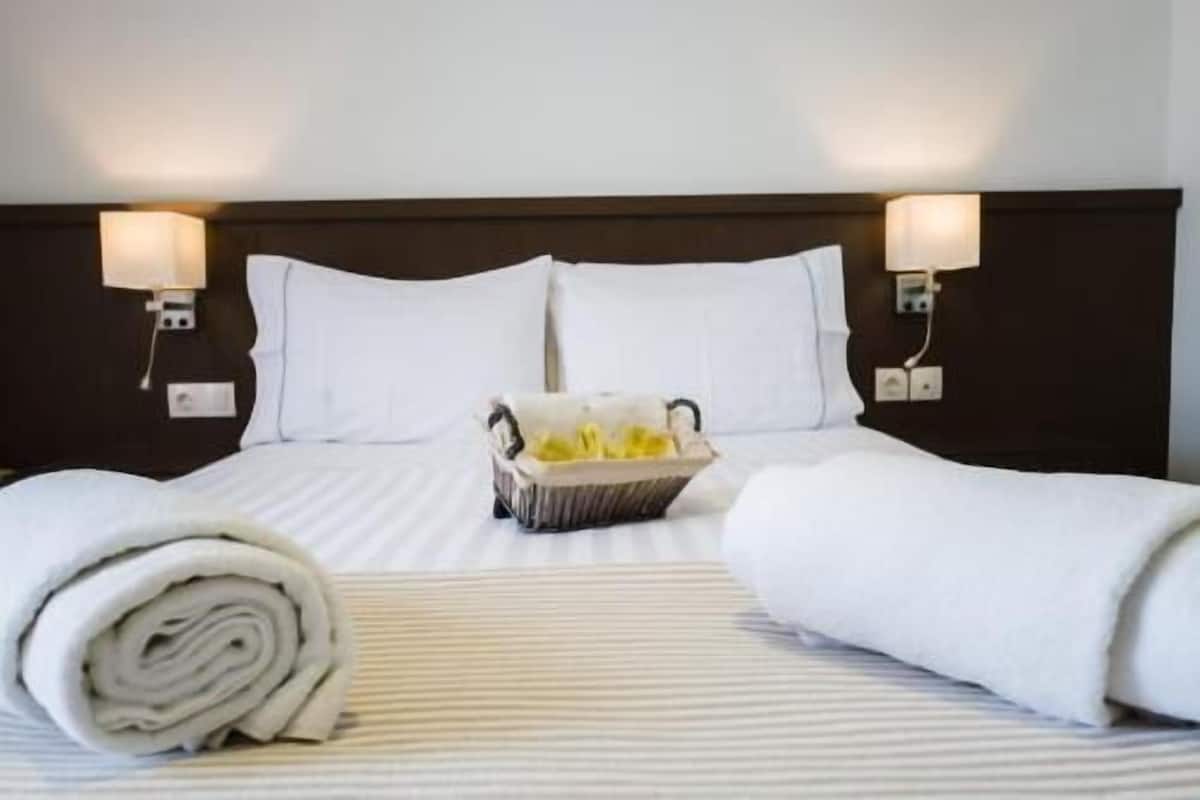 A hotel room with a neatly made bed, two bedside lamps, and a basket of toiletries.