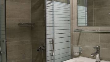 Un baño moderno con ducha envuelta en vidrio, un lavamanos blanco y un espejo grande.