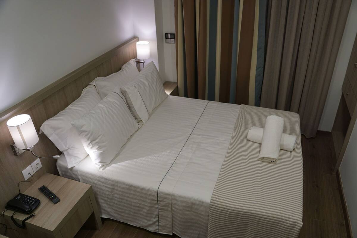 A hotel room with a bed, bedside lamps, a remote control, and a telephone on a nightstand.