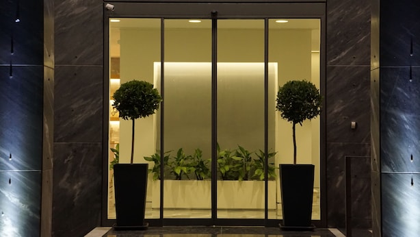 L’extérieur de l’hôtel Piraeus Port se distingue par sa façade moderne, ses grandes portes vitrées et les deux plantes en pot qui se trouvent devant l’entrée.