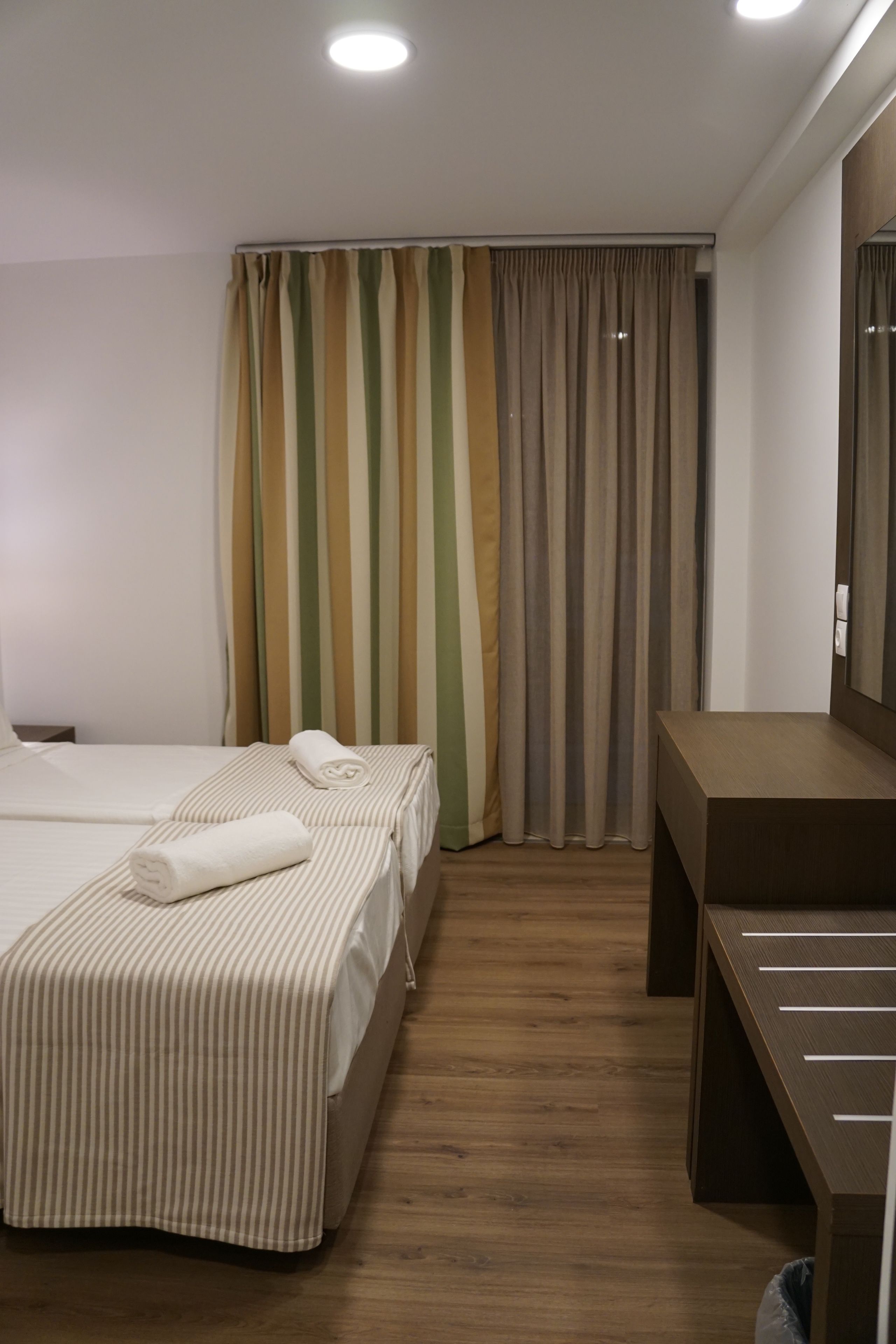 Habitación de hotel con dos camas, un escritorio de madera y un ventanal con cortinas a rayas.