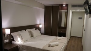 Une chambre d’hôtel avec un grand lit, deux tables de chevet avec des lampes, une armoire et un téléviseur fixé au mur.