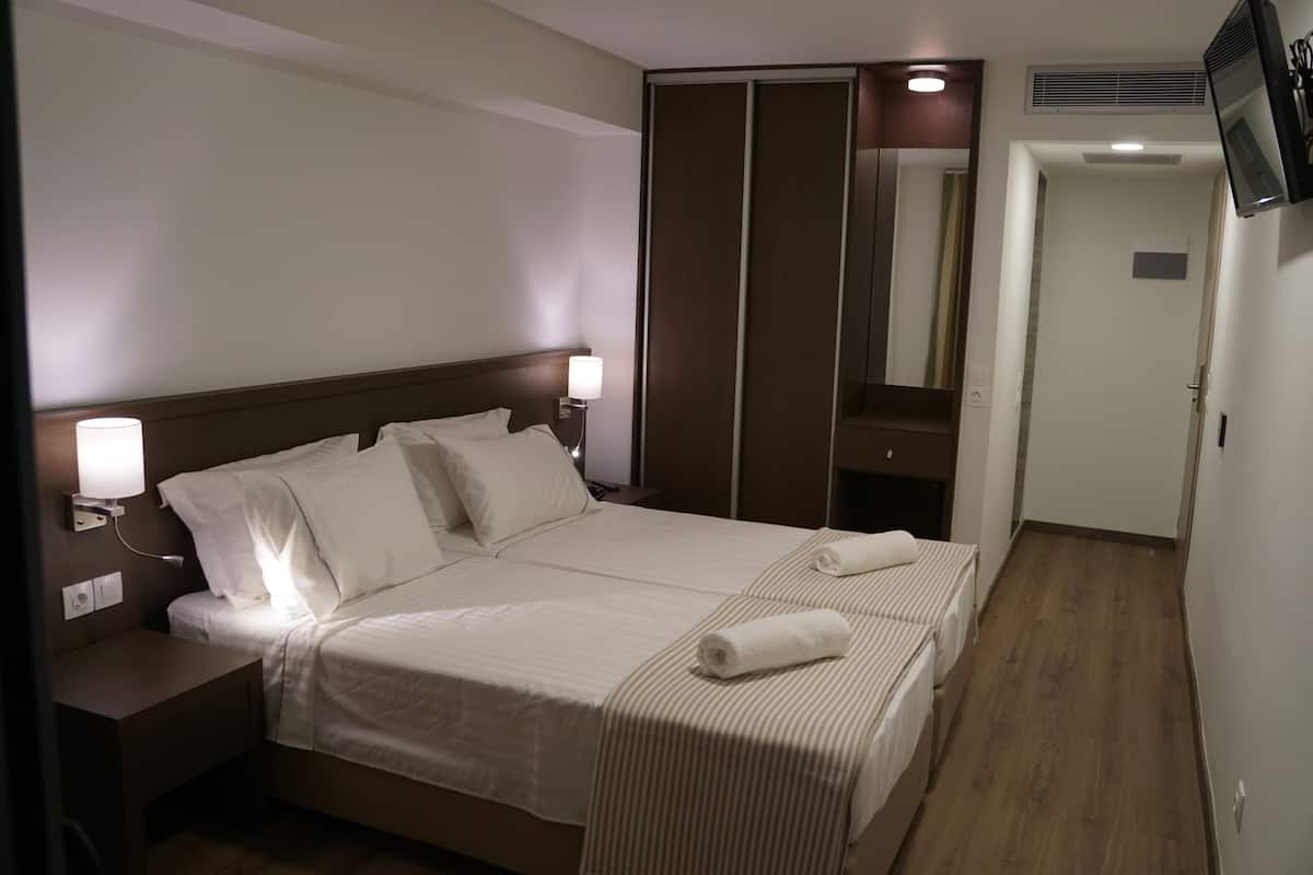 A hotel room with a large bed, two bedside tables with lamps, a wardrobe, and a television on the wall.