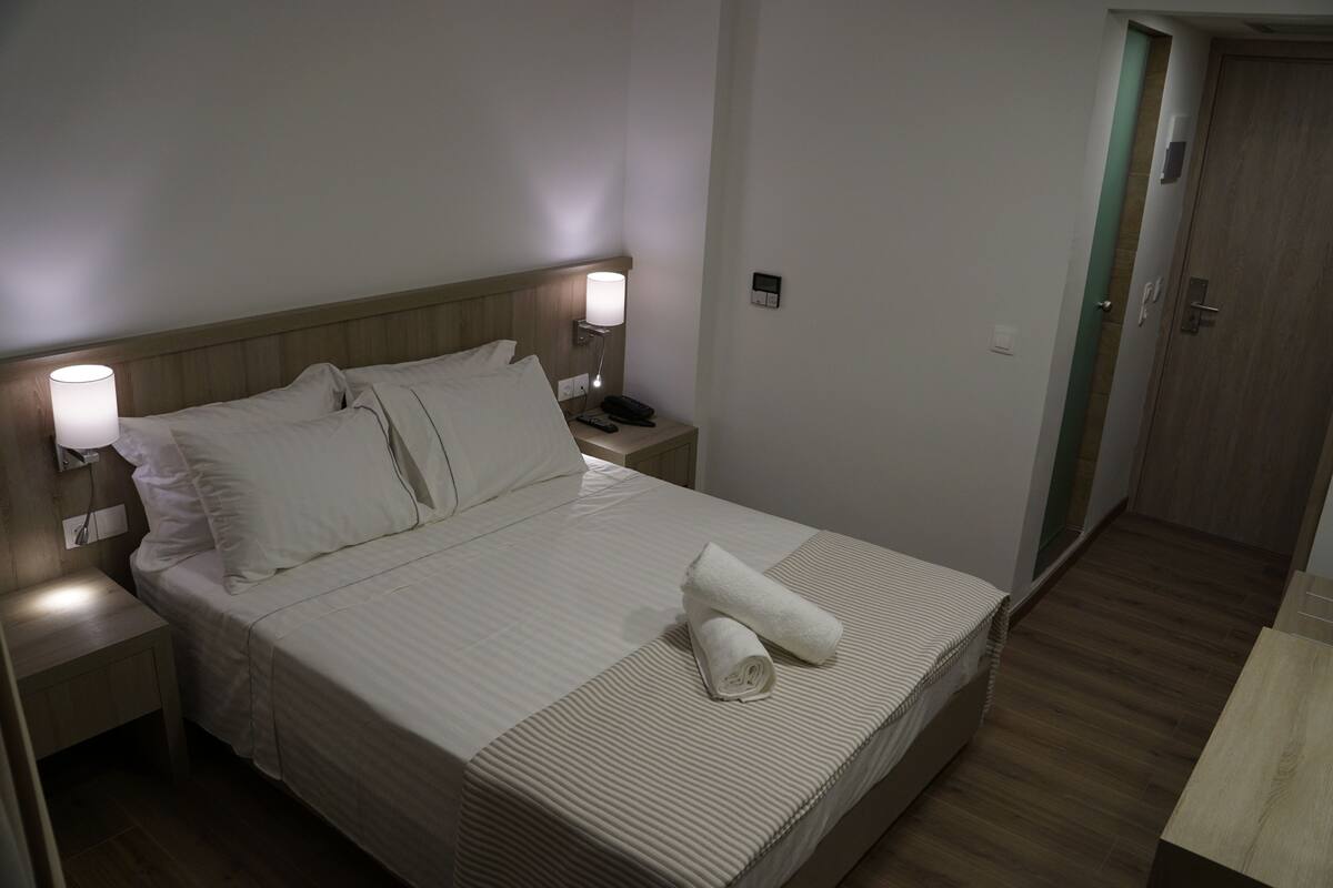 A neatly made bed with white linens, a bedside lamp, and a folded towel on the bed.