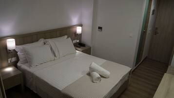 Una cama bien hecha con sábanas blancas, una lámpara de noche y una toalla doblada sobre la cama.