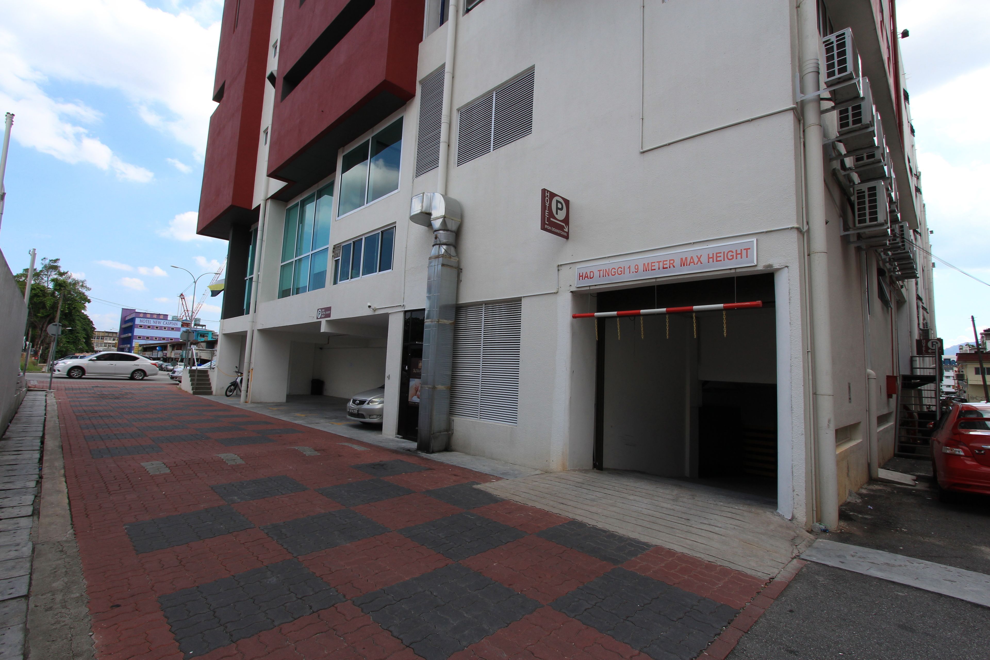Un edificio con entrada a un estacionamiento, una señal que indica una restricción de altura y pavimento a cuadros rojo y negro.