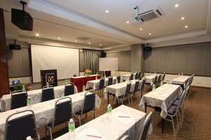 Un salón de conferencias con varias mesas, sillas y una pantalla de proyección.