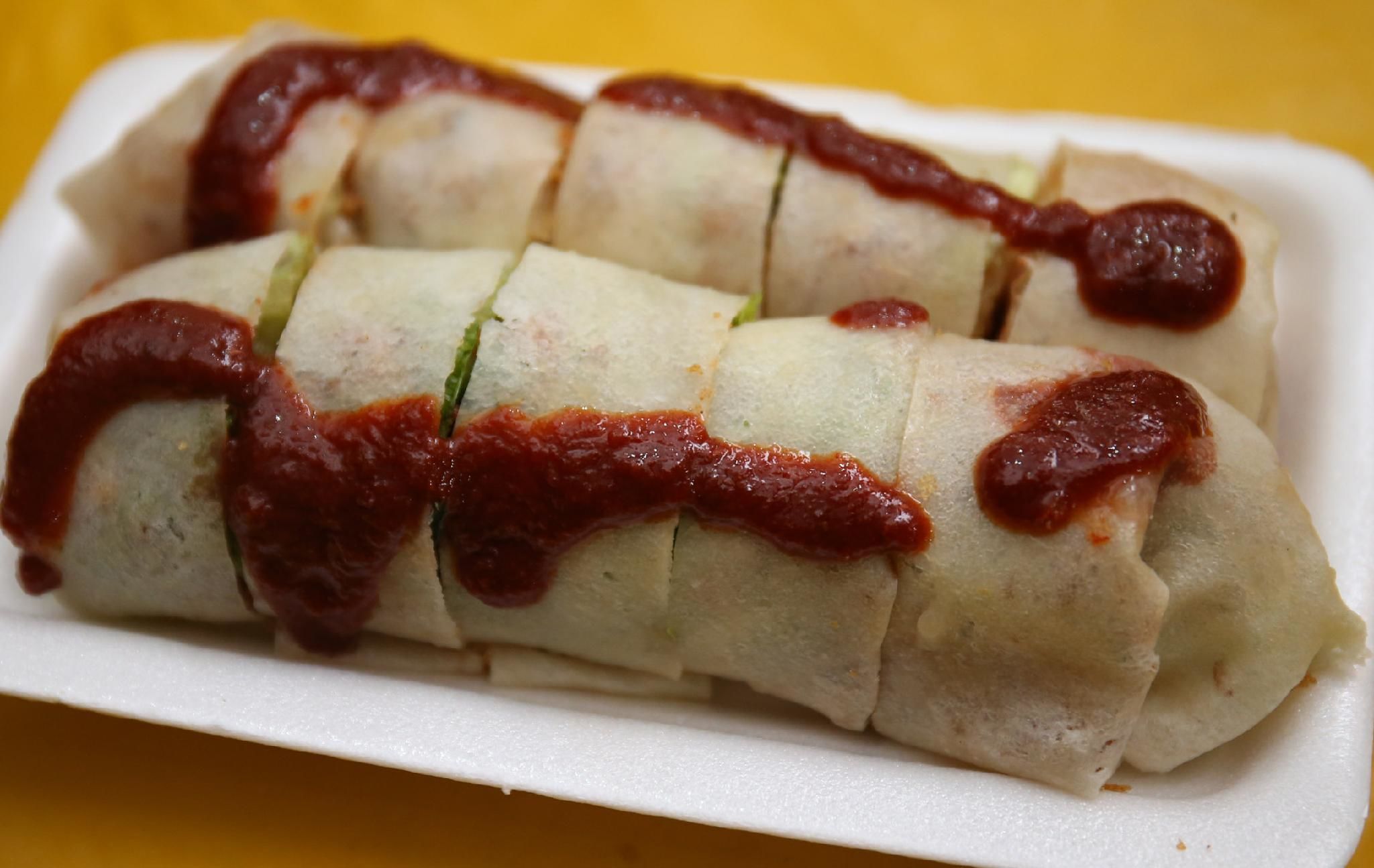 Un plato rectangular blanco con cuatro rollos de primavera cubiertos de salsa roja.