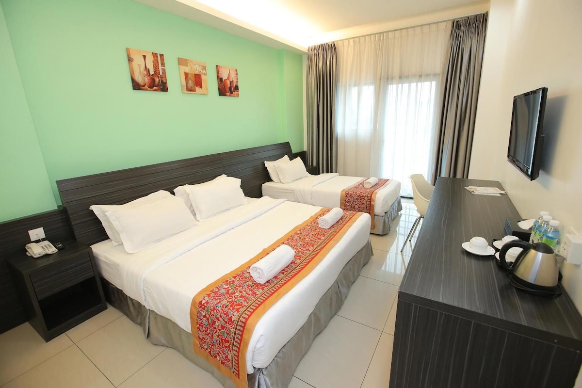 Camera d'albergo con due letti, una scrivania con un bollitore, una sedia e una televisione.
