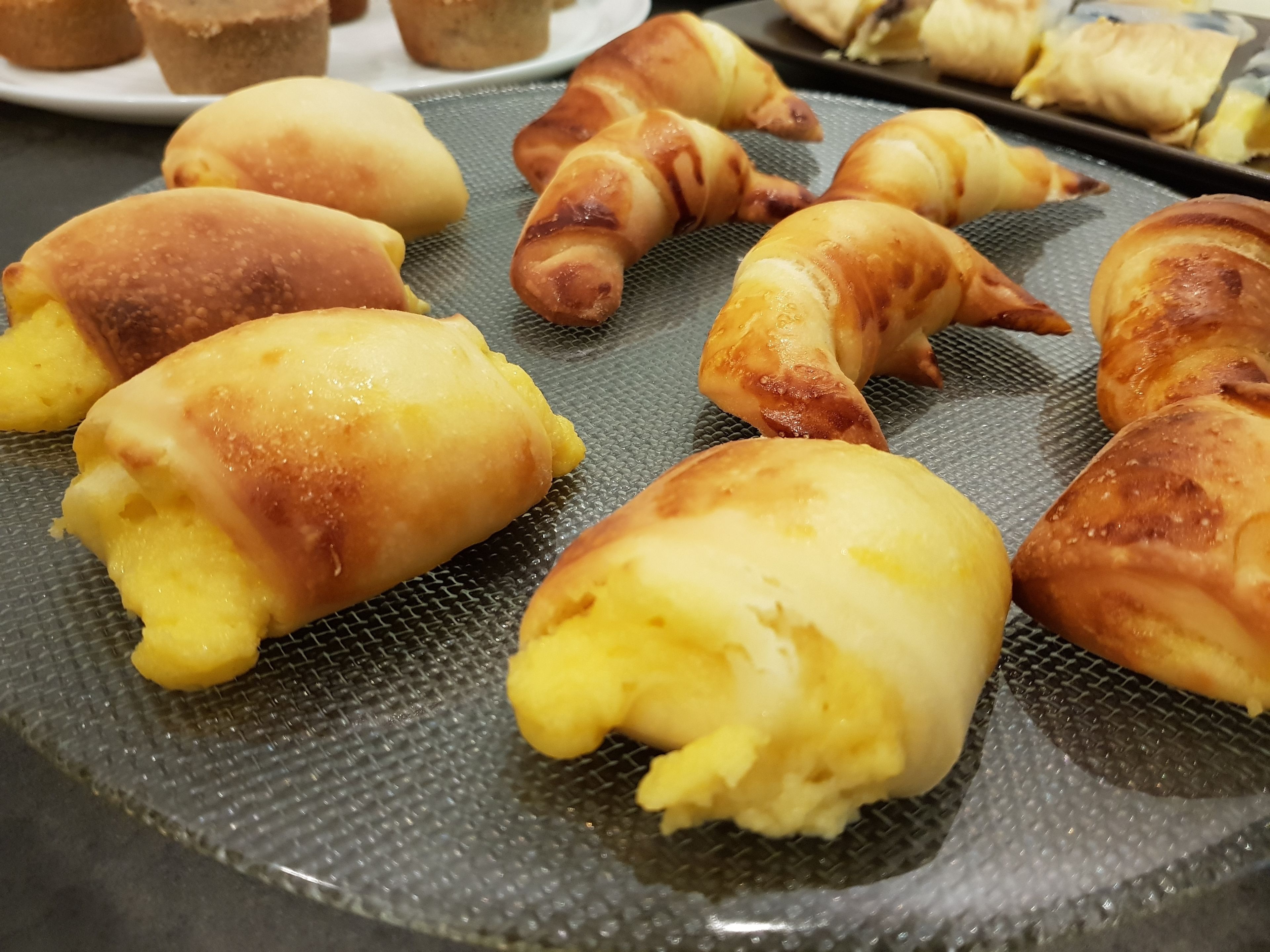 A tray of baked goods, including croissants and rolls, on a metal surface.