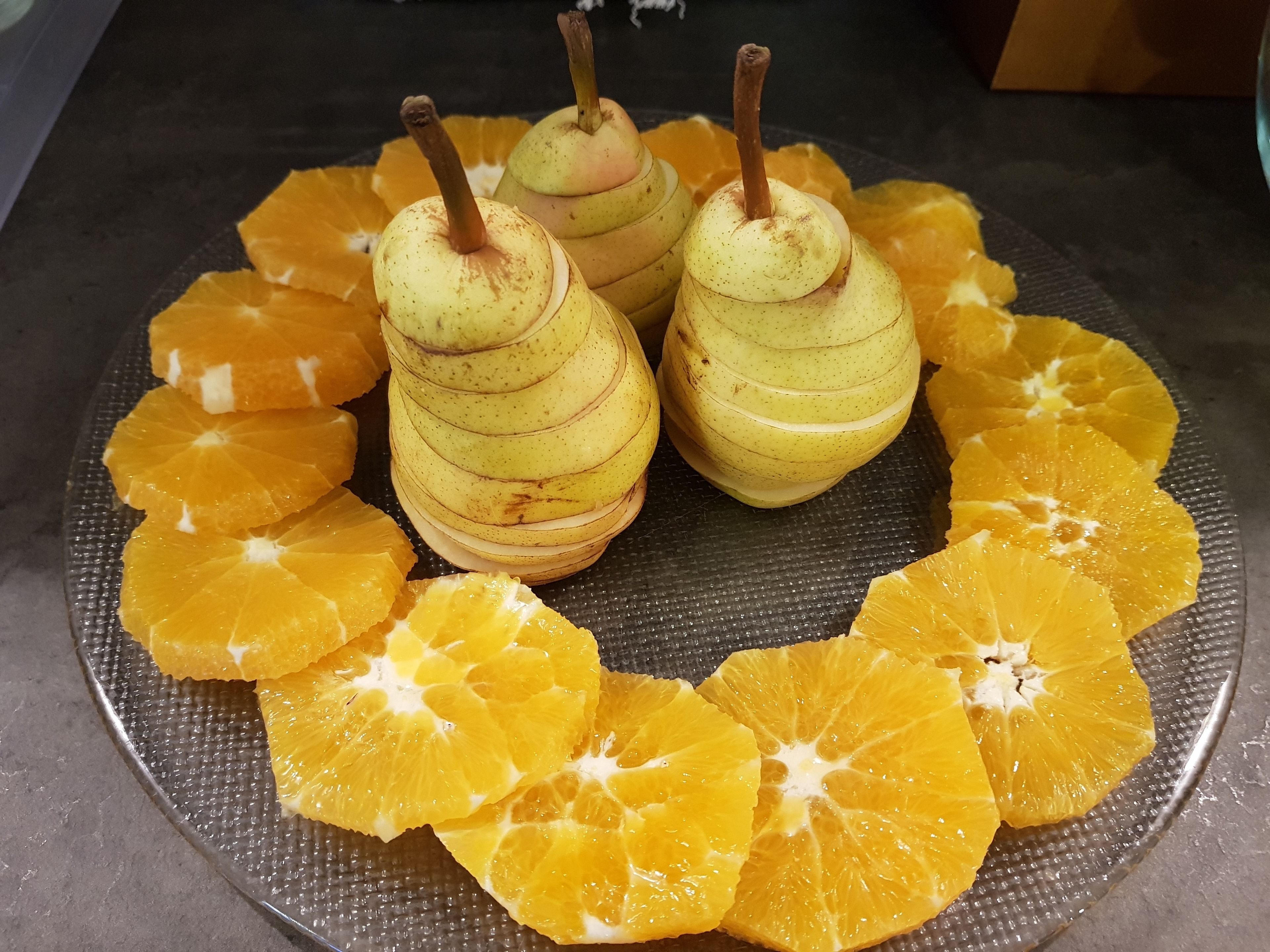 Ein Teller mit Scheiben Orangen und Birnen auf einer strukturierten Oberfläche.