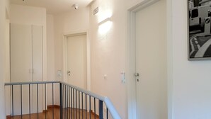 A staircase with a metal railing, wooden steps, and white walls. There are three doors, one with a light switch and another with a thermostat.