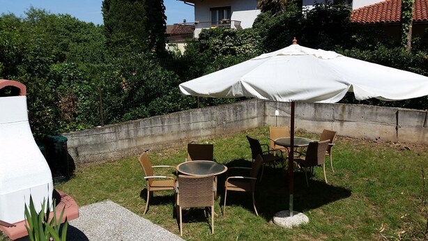 An outdoor patio with wicker chairs and a round table, a white umbrella, and a concrete wall.