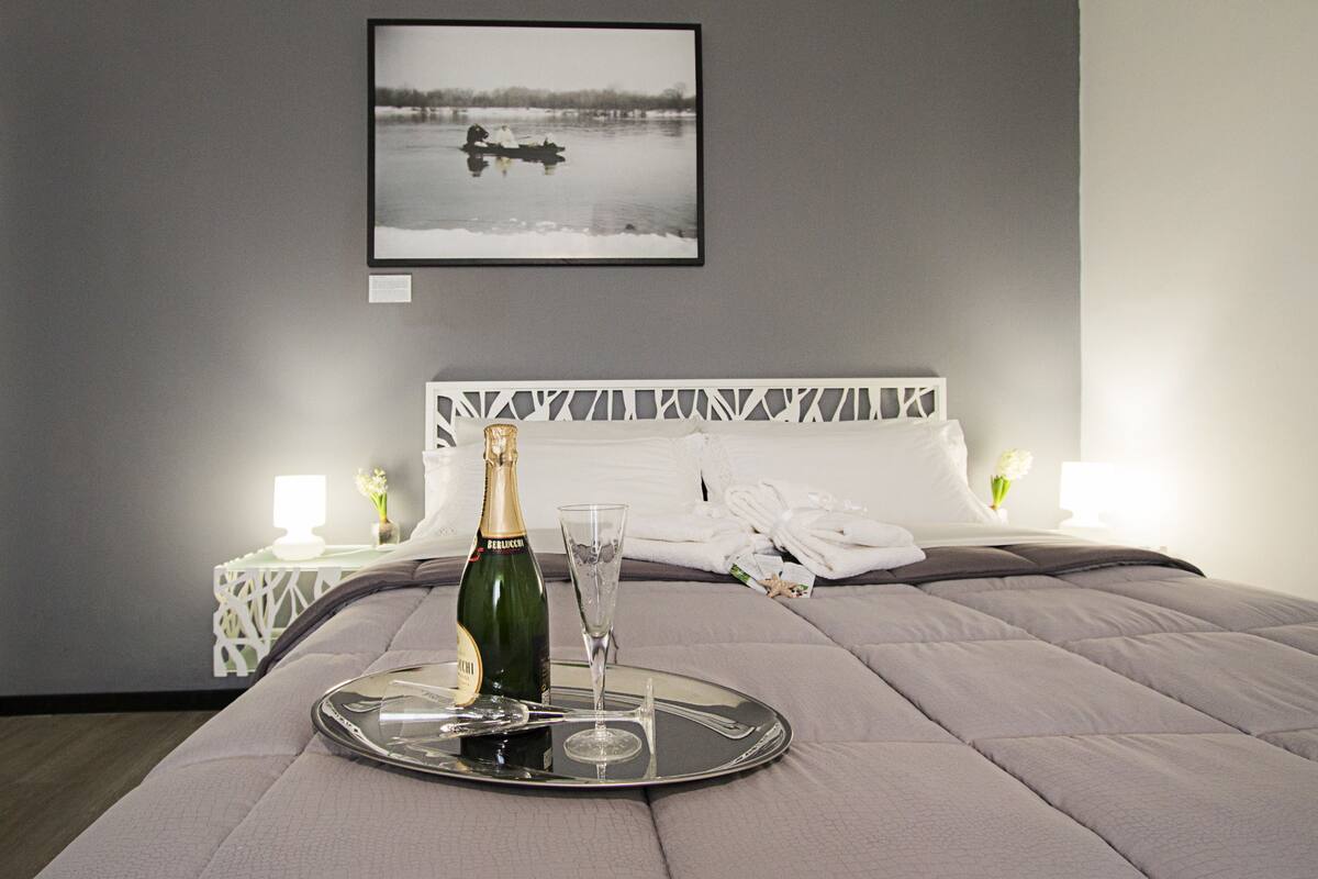 A neatly made bed with a tray holding a bottle and a glass, a framed picture on the wall, and a white headboard.