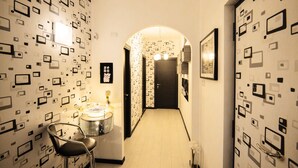 A hallway with patterned wallpaper, a chair, a small table with a vase, and framed pictures on the walls. - City Lights Rome (Rome)