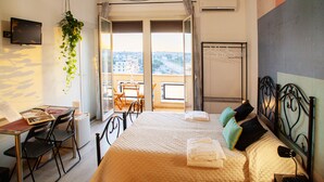 A hotel room with a bed, a desk, a chair, a TV, and a balcony with a view. - City Lights Rome (Rome)
