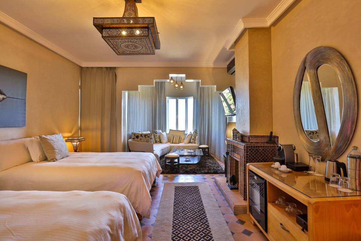 A hotel room with a large bed, a sofa, a coffee table, a TV, and a mirror.