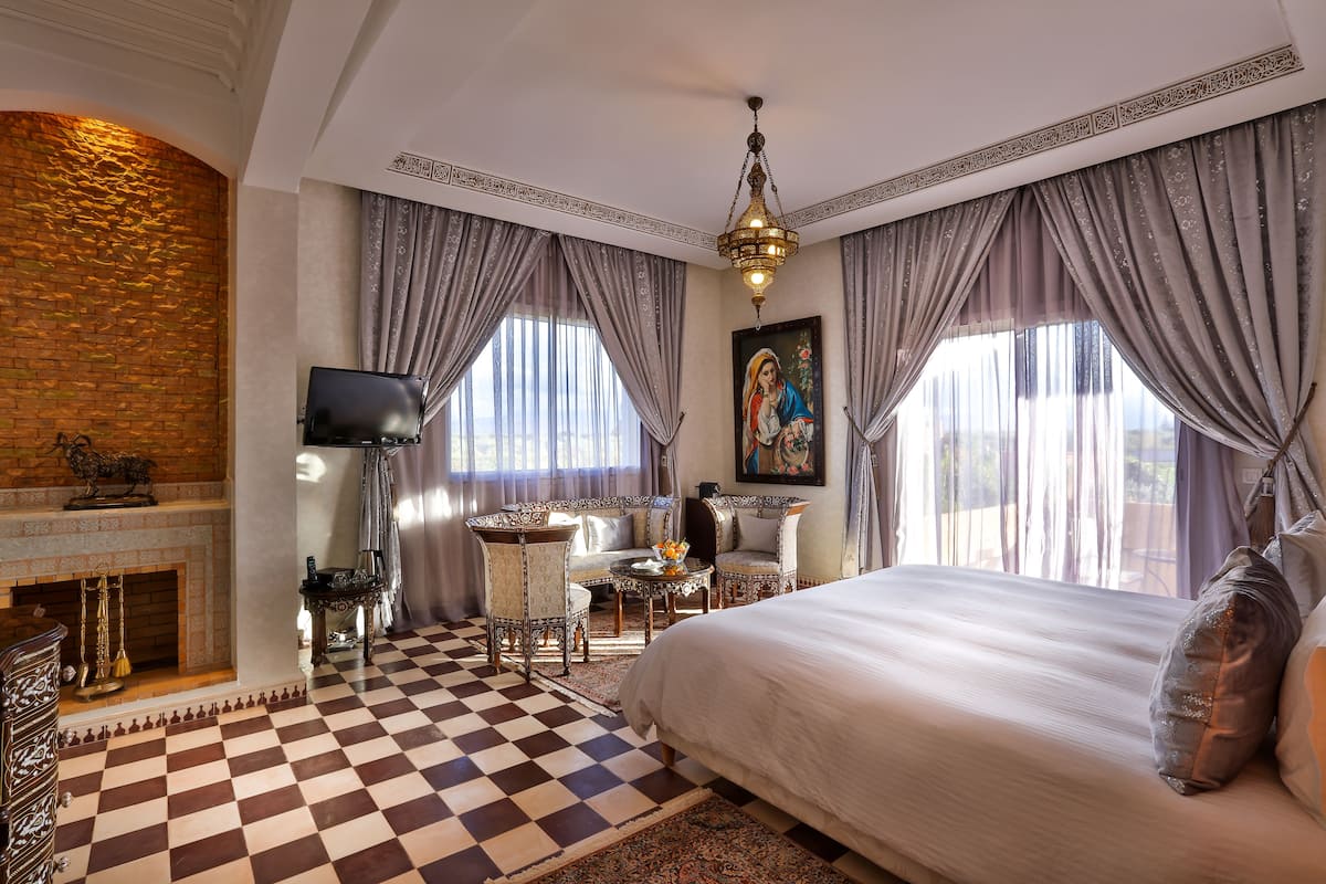 A hotel room with a checkered floor, a fireplace, a bed, a dining table, and a chandelier.