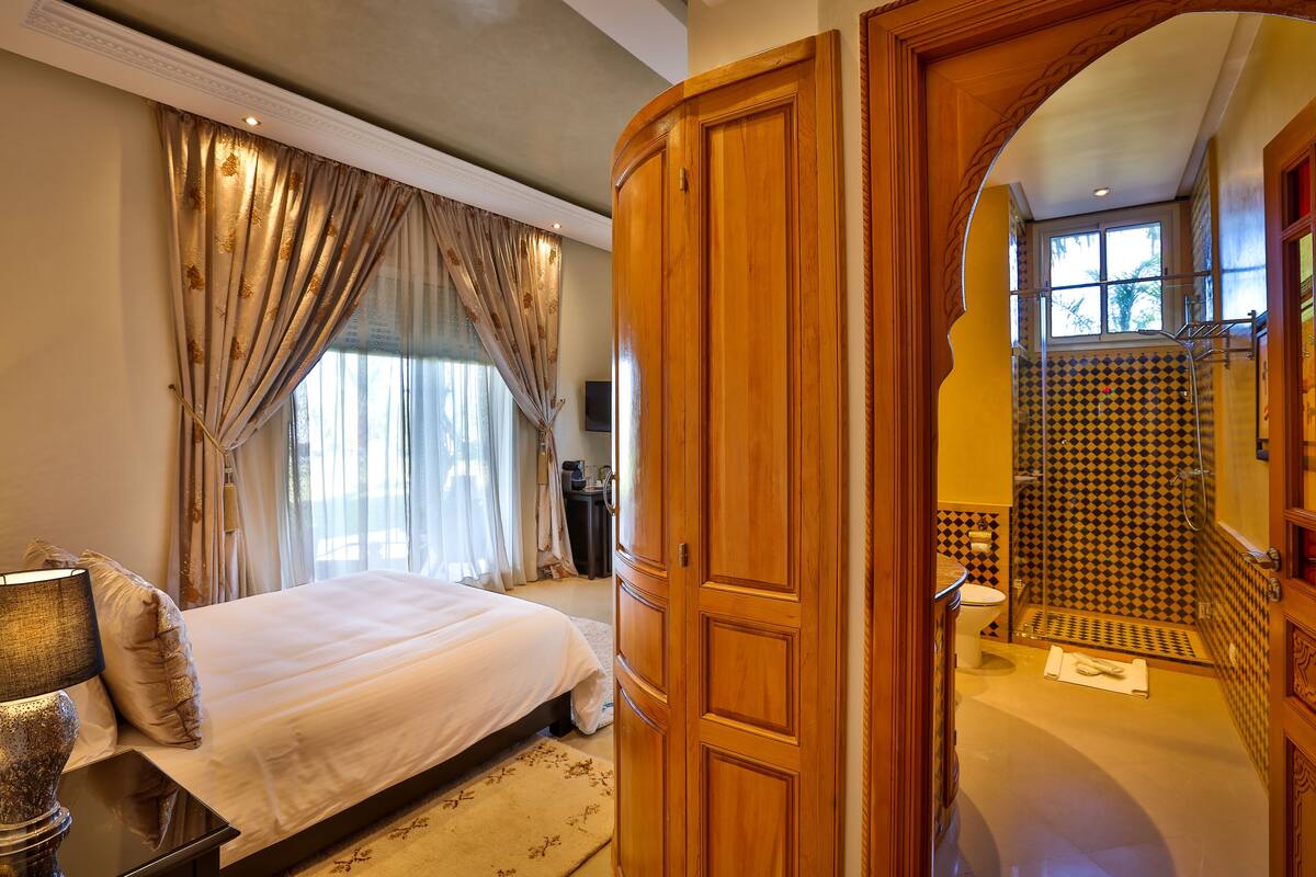 A bedroom with a large bed, a bedside table, and a wooden door leading to a bathroom with a shower and tiled walls.
