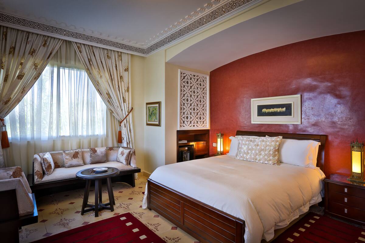 A hotel room with a large bed, a sofa, a small table, and a decorative wall panel.