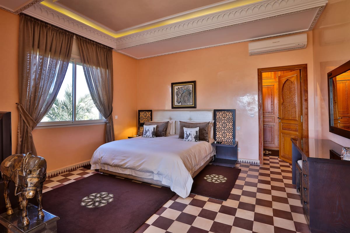 A bedroom with a large bed, a nightstand, a decorative wall panel, and a window with curtains.