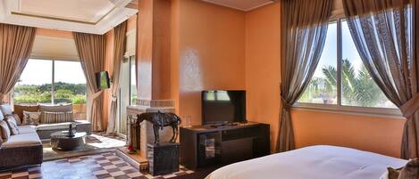 A hotel room with a large bed, a sofa, a TV, and a view of the outdoors.