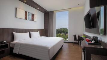 A modern hotel room with a large bed, a desk, a chair, a flat-screen TV, and a large window offering a view of the outdoors.