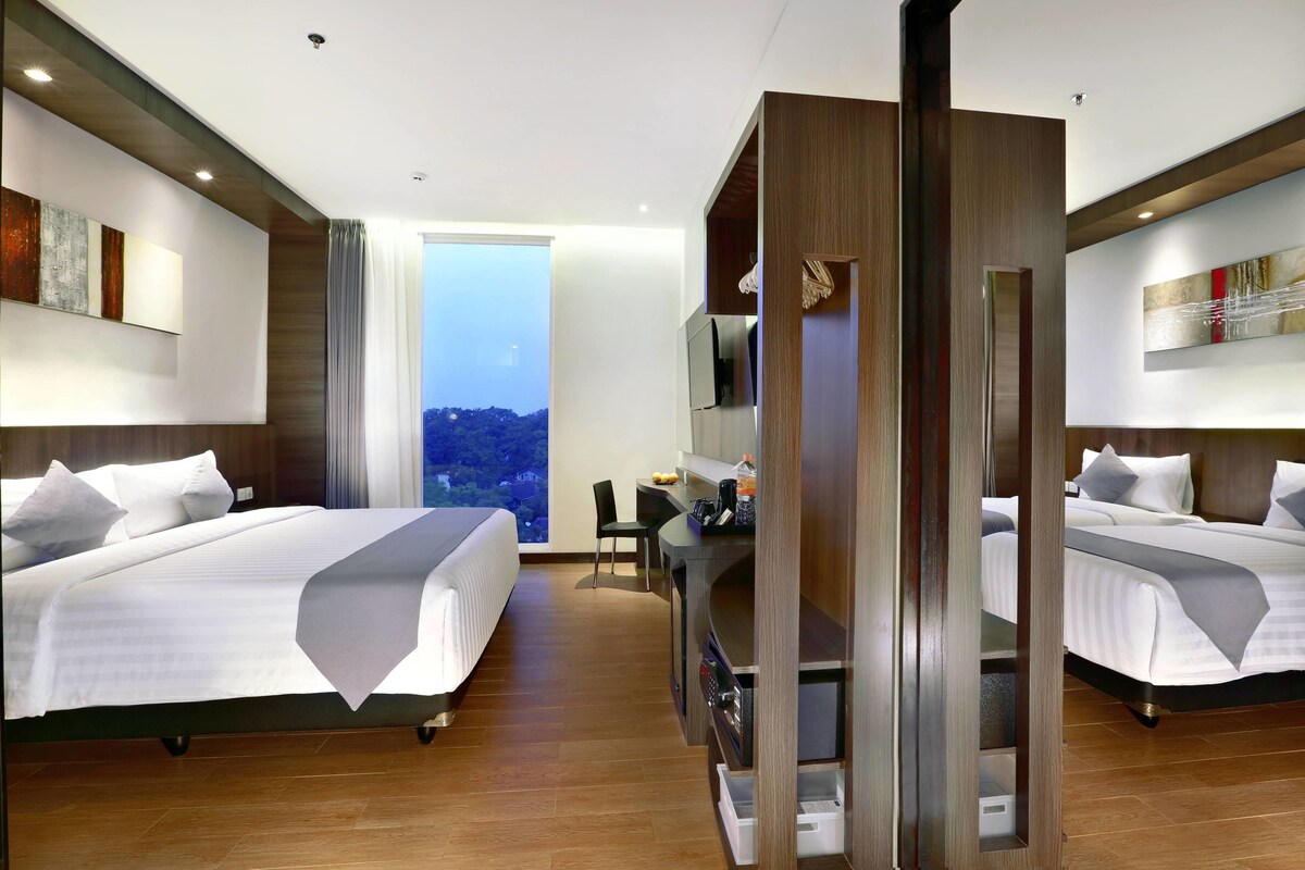 A hotel room with two beds, a desk, a TV, and a view of the city.