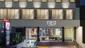 Exterior del NEO Hotel con un diseño moderno, que incluye una entrada bien iluminada, una escalera que conduce al vestíbulo y un cartel con los servicios del hotel.