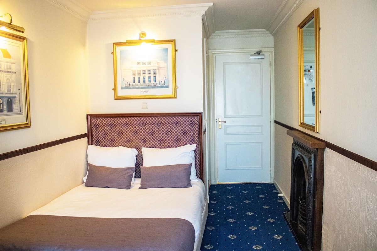 Een hotelkamer met een bed, een lijst met een foto aan de muur, een deur en een spiegel.