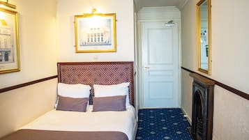 A hotel room with a bed, a framed picture on the wall, a door, and a mirror.