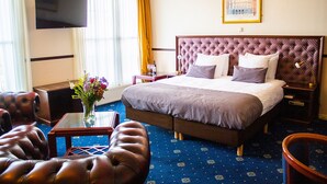 Une chambre d’hôtel avec un grand lit, une télévision, un bureau agrémenté d’un vase de fleurs et un fauteuil en cuir.