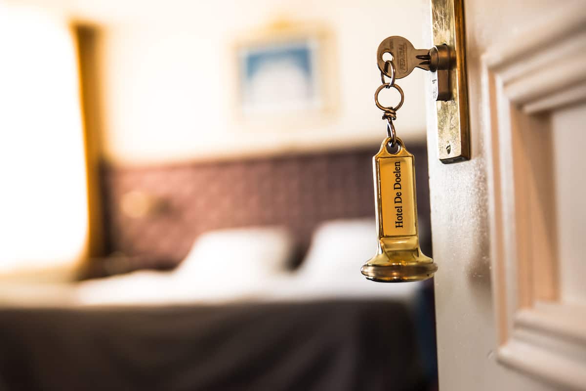 Een hotel sleutel met 'Hotel Doelen' gegraveerd, aan een deurklink hangend.