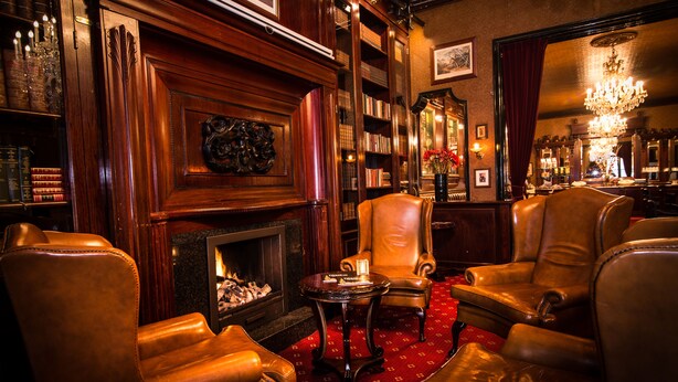 Un salon confortable avec des fauteuils en cuir, une cheminée, des étagères et un bar.