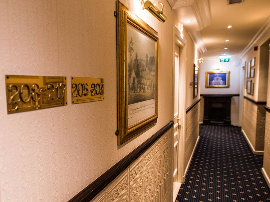 Un pasillo con cuadros y placas en la pared, una alfombra estampada y una puerta al final.
