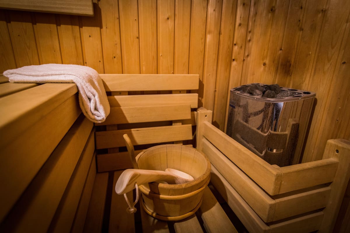 Een houten saunabank met een handdoek eroverheen, een houten emmer en een sauna-kachel.